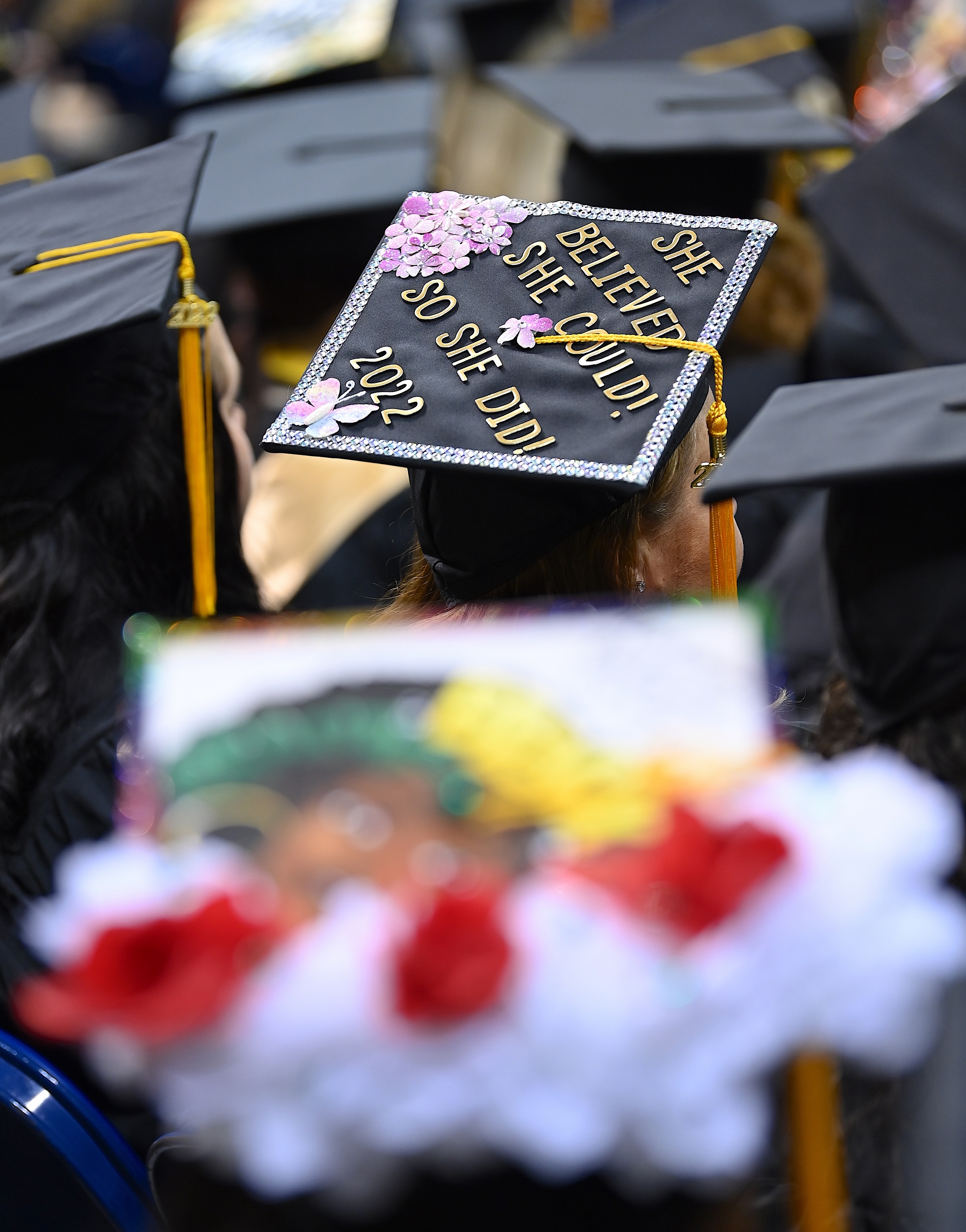 A graduation cap in the background of the photo that says "She believed she could! So she did! 2022"