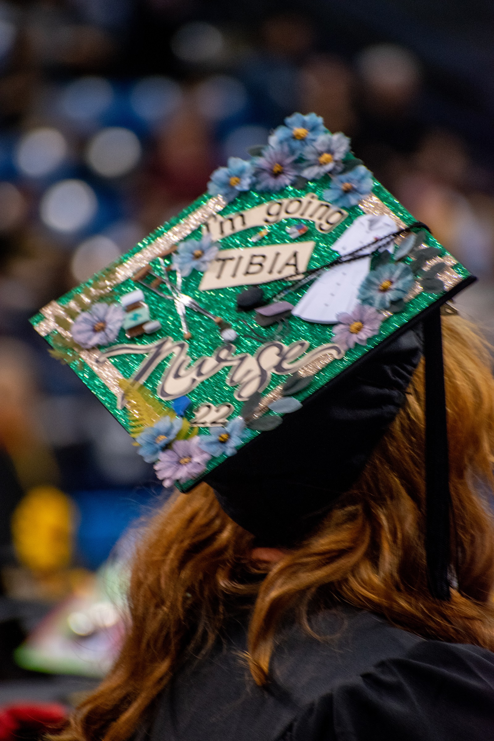 A graduation cap decorated with flowers and miniature medical items. The cap says "I'm going tibia nurse."