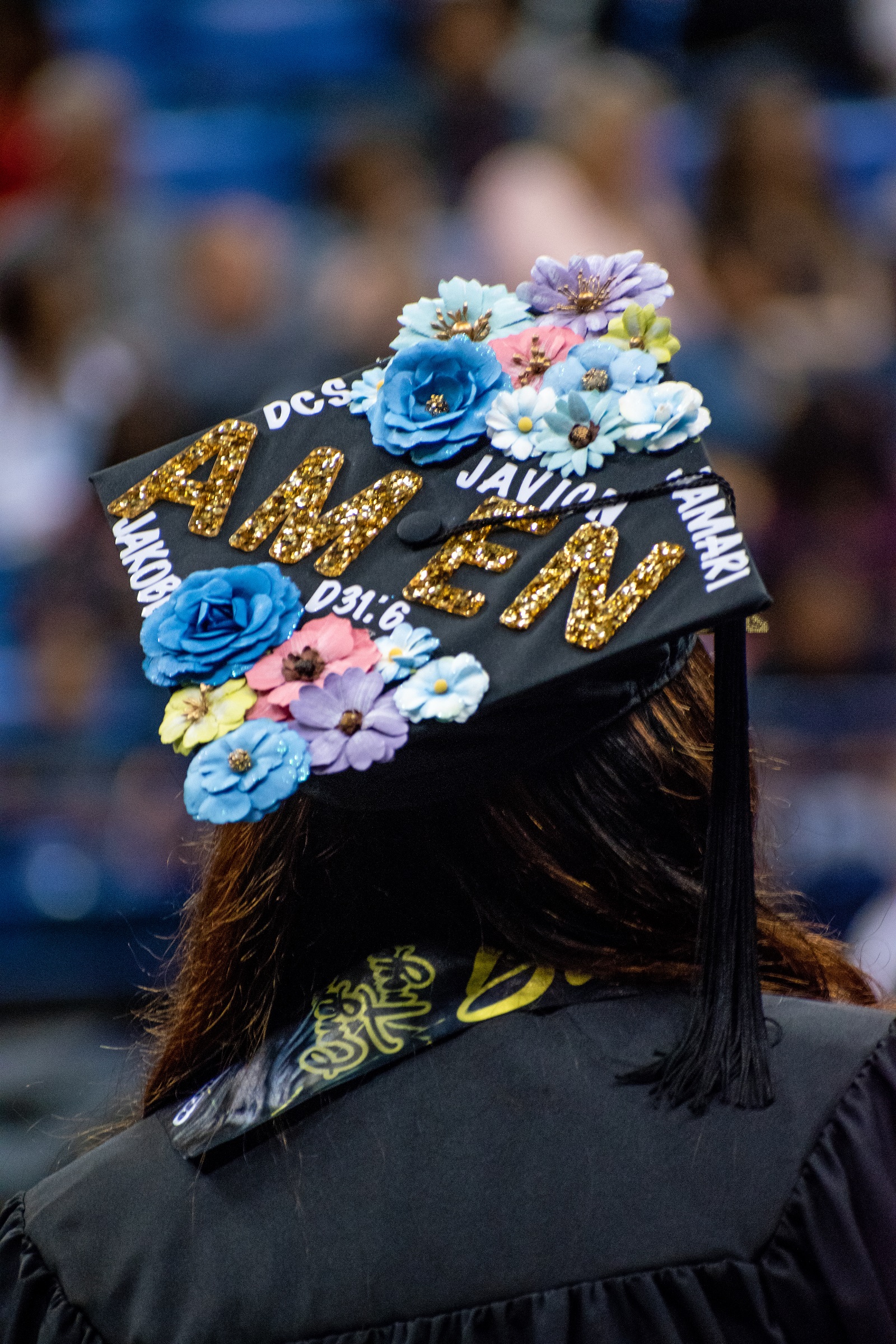 A graduation cap decorated with flowers. It has several names on it and the word "Amen" in all capital letters.