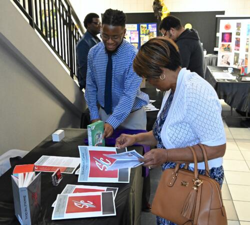 A woman flips through a pamphlet at a graduate's table as he looks on.