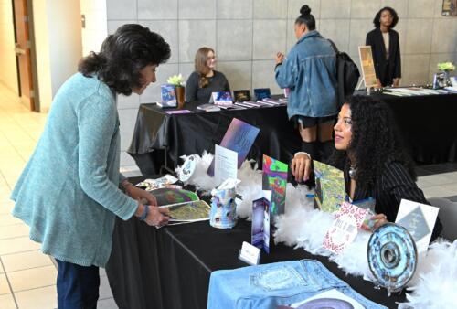 A woman leans over a table and talks to a graduate seated behind it.