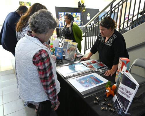 A graduate leans on her hands on the table while talking with visitors during the showcase.