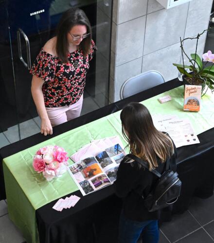 A photo taken from overhead of a women standing at a graduate's table looking at her work.