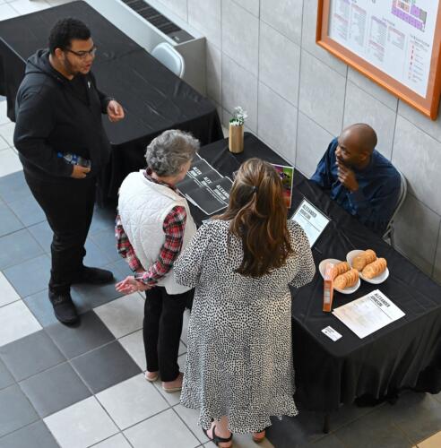 Photographed from overhead, a graduate talks with two women and a man at his table.
