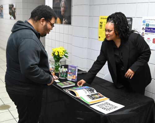 A graduate points out details of her work to a man at her table.