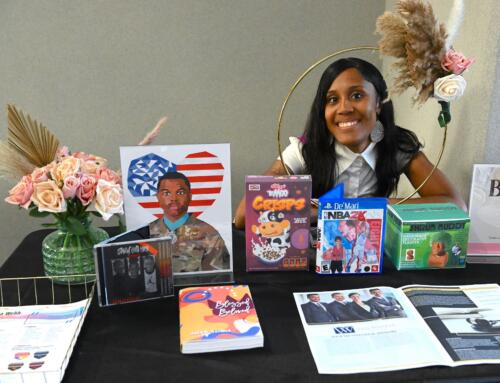 A graphic design student sits at a table where her work is displayed.