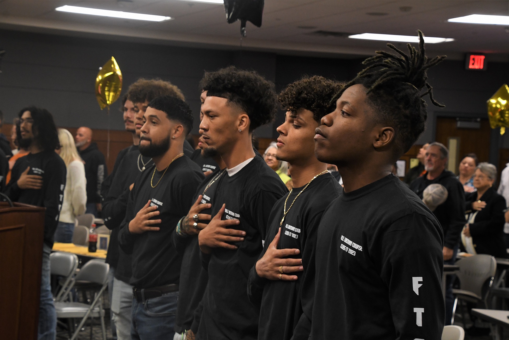 Graduates stand in a row with their hands over their hearts during the playing of the national anthem.