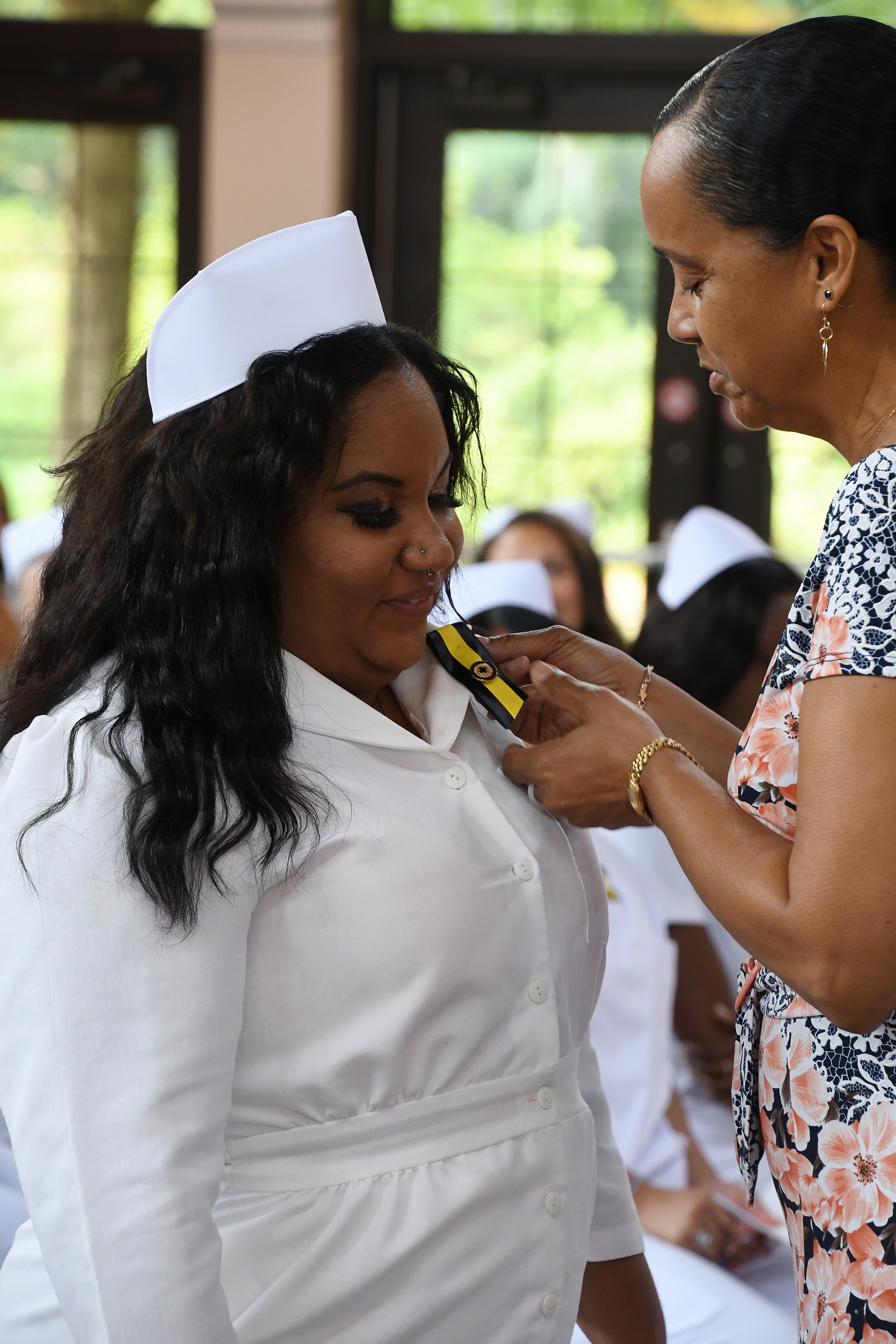 A graduate looks down and smiles as her pin is placed on her uniform.