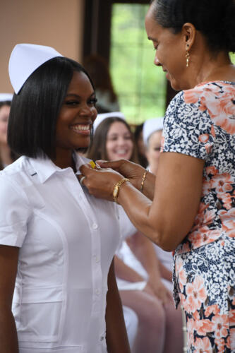 A graduate smiles as her pin is placed on her uniform.