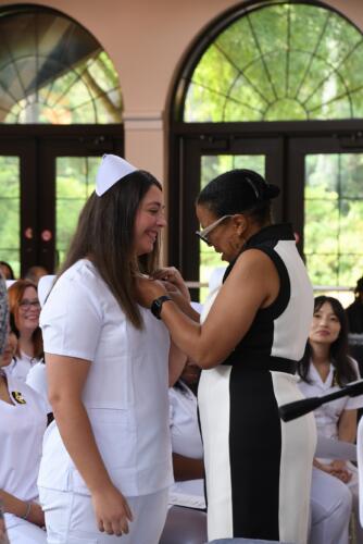 A graduate smiles as her pin is placed on her uniform.