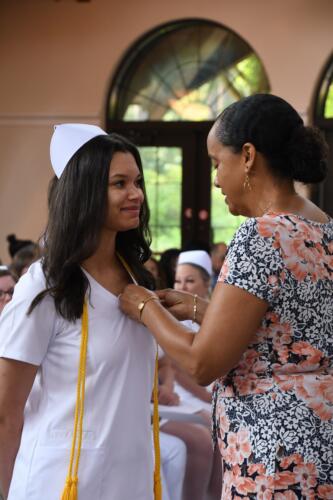 A graduate wearing a gold cord smiles as her pin is placed on her uniform.