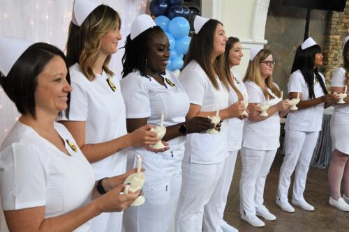 LPN graduates stand in a line holding lit candles in holders that look like lamps.