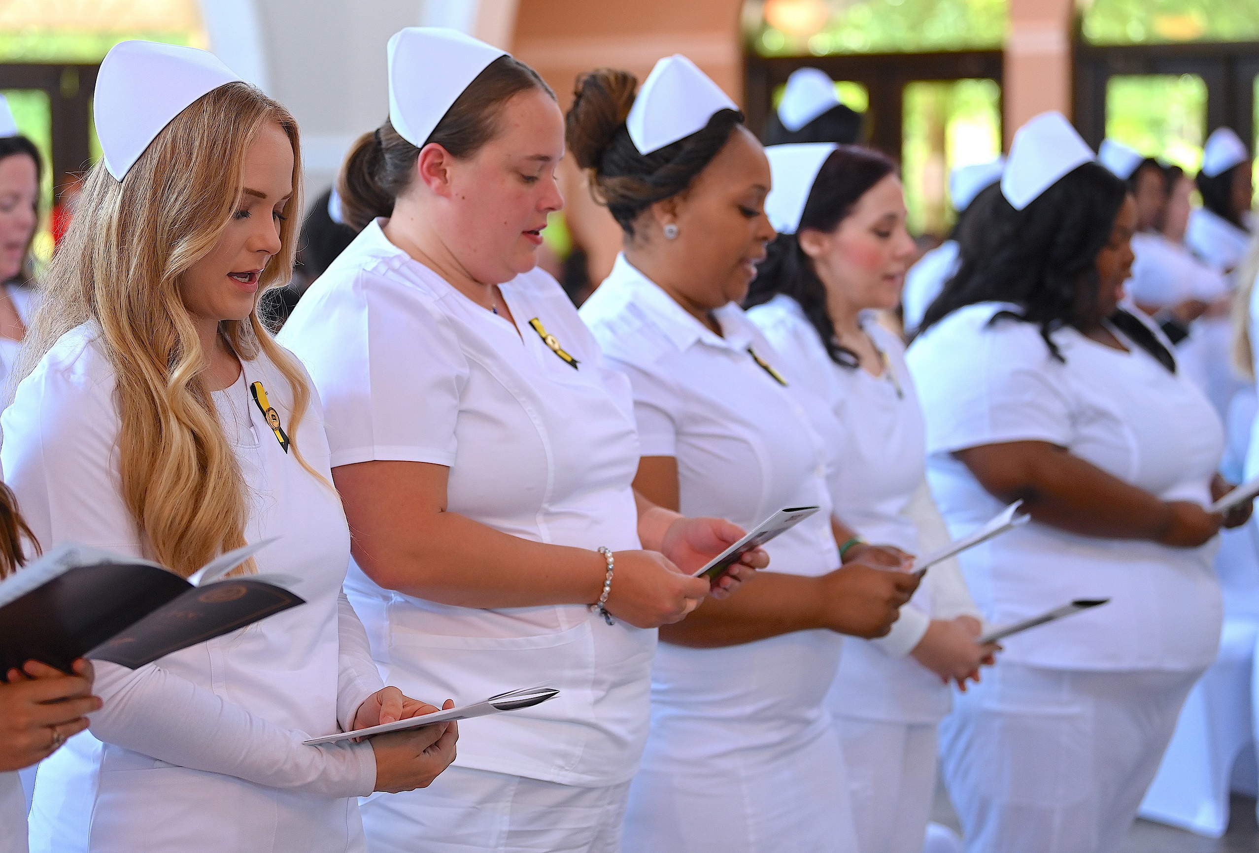 A row of seated nursing graduates read from the program at the pinning ceremony.