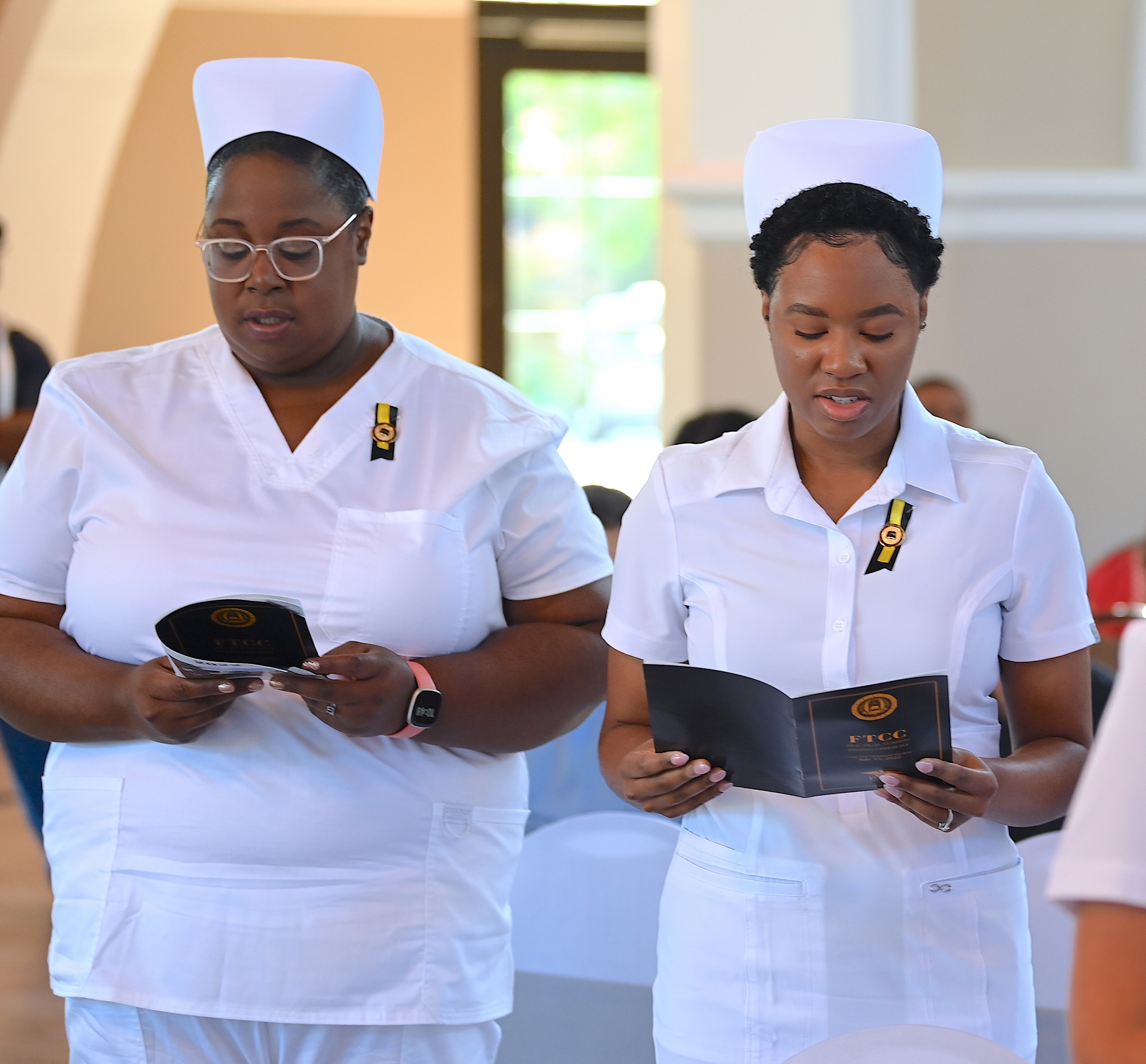 Two standing nursing graduates read from the program during the pinning ceremony.