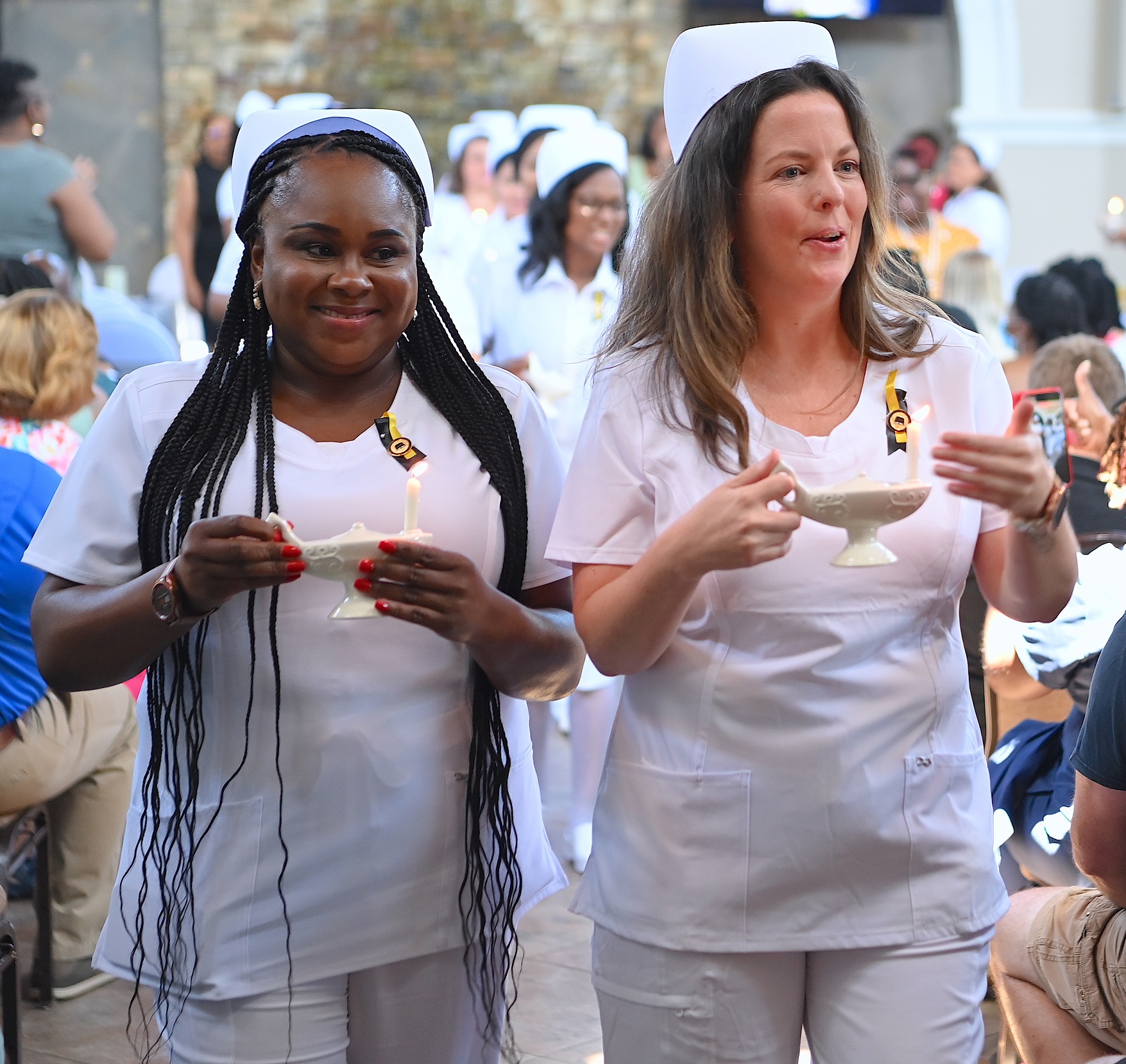 Two nursing graduates walk side-by-side with their lamps lit.