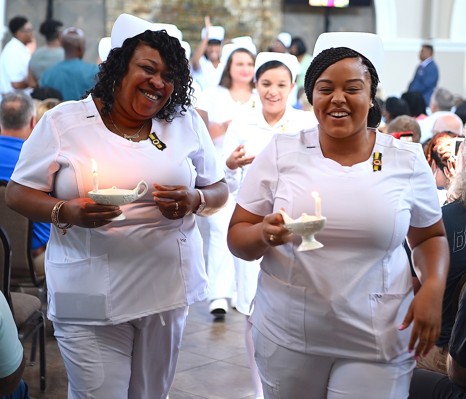 Two nursing graduates smile at the camera as they walk side-by-side with their lamps lit.