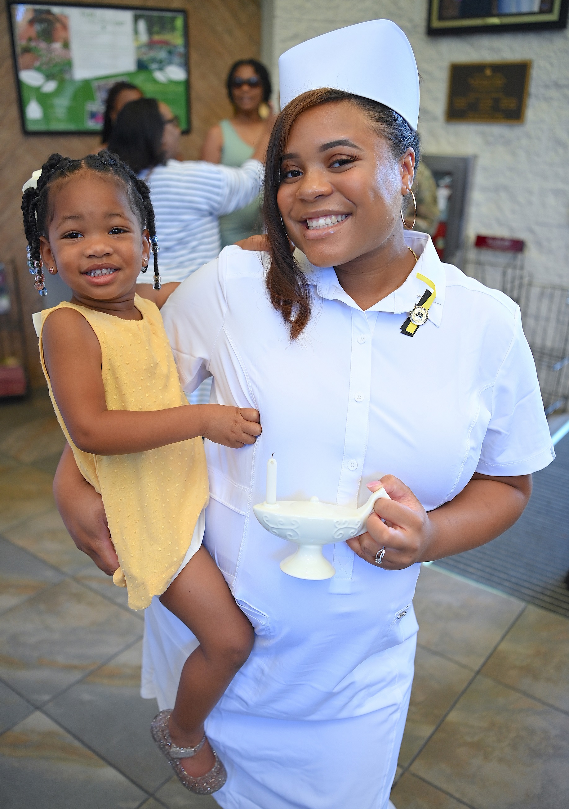 A nursing graduate holds a young girl with one hand and holds her candle lamp in the other hand.